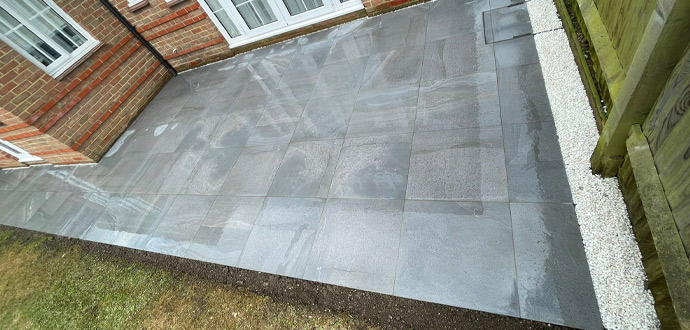 Patio area with large gray tiles and grass border, featuring modern outdoor design elements.