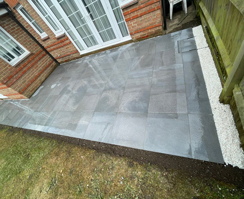 Patio area with modern gray tiles and white gravel border, featuring lush green grass nearby.