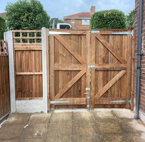 wooden garden gates with a lock, surrounded by a fence and greenery