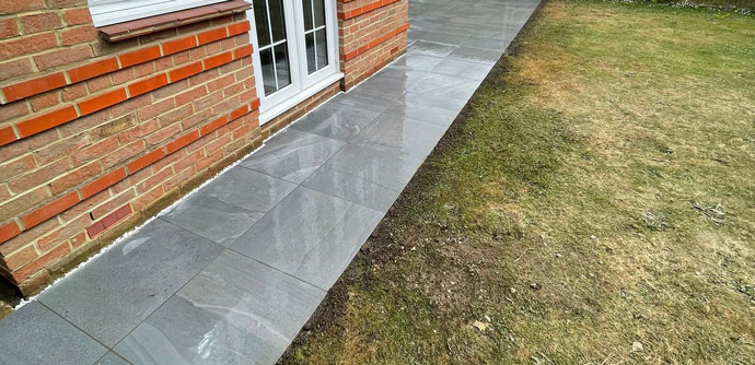 paved walkway beside a brick house with a lawn, showcasing smooth gray tiles and a clean modern design