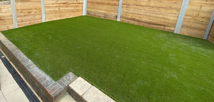 Artificial grass area with a surrounding border, enclosed by wooden fencing.