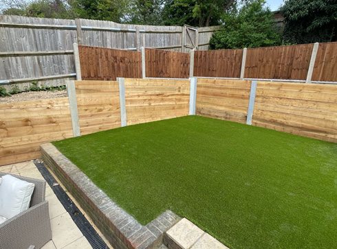 Artificial grass area enclosed by wooden fences, featuring a neatly manicured green lawn, suitable for outdoor leisure and gardening.