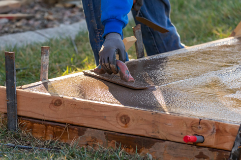 Person smoothing wet concrete with a trowel on a wooden form, showcasing a construction or DIY process.