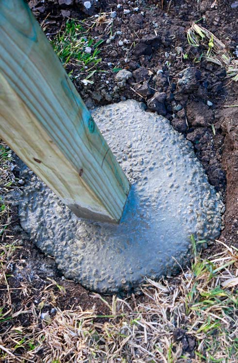 Wooden post anchored in concrete mix on a grassy surface, illustrating a construction or landscaping setting.