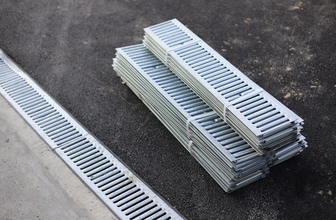 stack of metal drainage grates on a construction site next to a channel drain