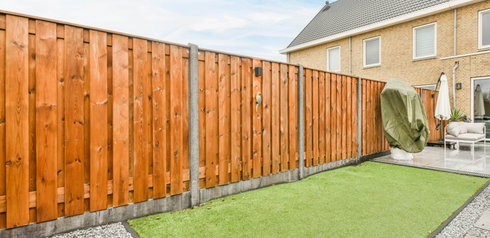 Wooden fence surrounding a landscaped backyard with artificial grass and patio area, featuring modern outdoor furniture and planters, ideal for garden relaxation.