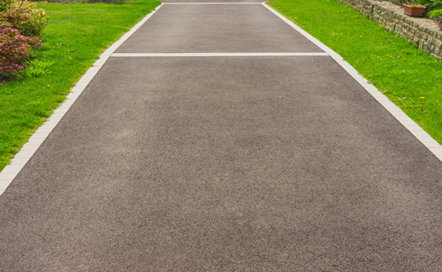 a well-maintained asphalt pathway leading through lush green grass and bordered by shrubs and stones