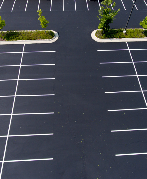 Aerial view of a nearly empty parking lot with clearly marked white lines and a few trees along the edges.