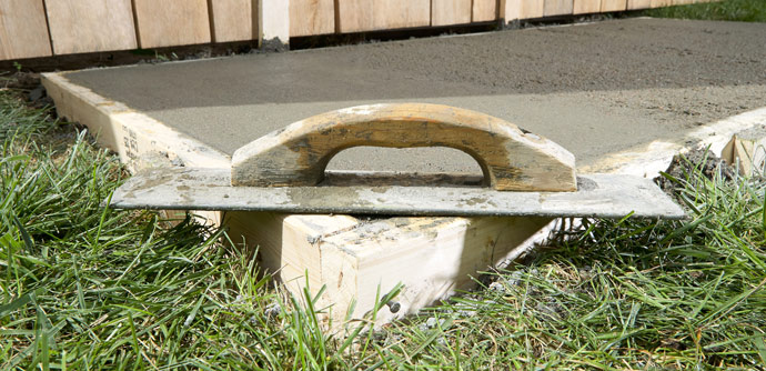 Concrete trowel resting on freshly laid concrete surface with grassy edges. Ideal for outdoor construction projects.