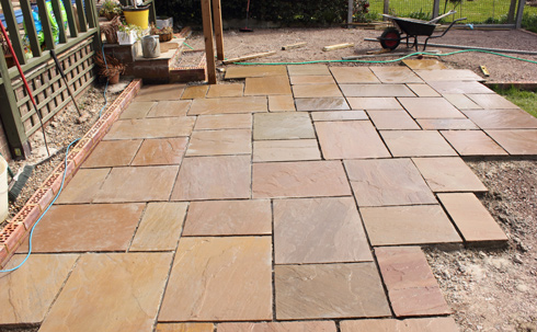 Newly laid stone patio with irregularly shaped flagstones arranged on a garden surface, showcasing a blend of earthy tones. Perfect for outdoor landscaping.