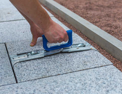 A person using a tool to adjust and align large stone paving slabs, showcasing a close-up of the hand grip and the stone surface.