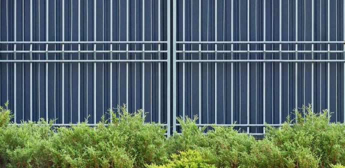 Metal fence with vertical bars against a background of green shrubs, showcasing a modern outdoor design.