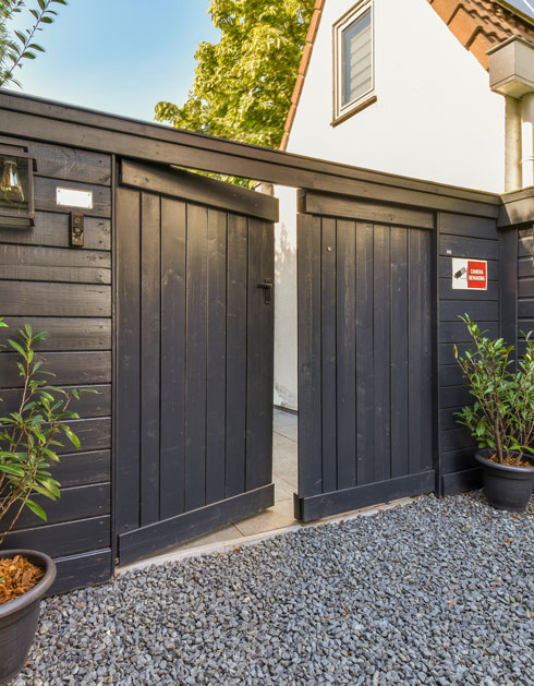 black garden gate opened with potted plants and gravel walkway, modern residential entryway