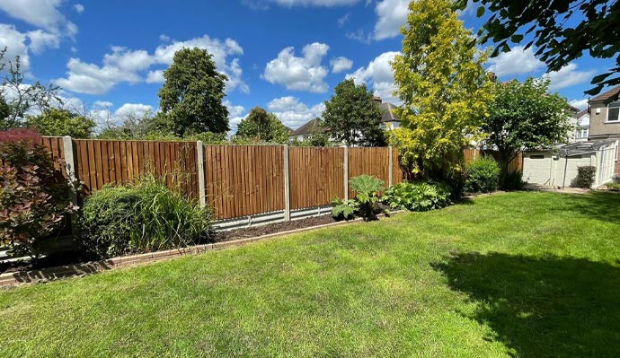 A lush green garden with a wooden fence, vibrant plants, and a clear blue sky with fluffy clouds. Ideal outdoor space for relaxation and gardening.